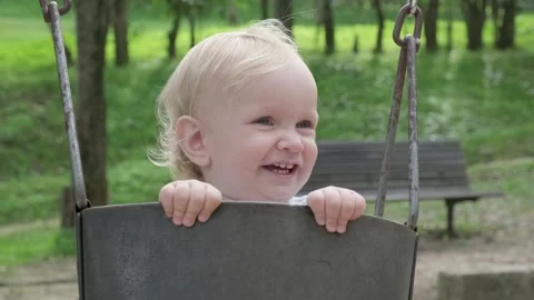 Small caucasian boy smiling while swinging on a swing on the kid's playground. Stock Footage 303047248