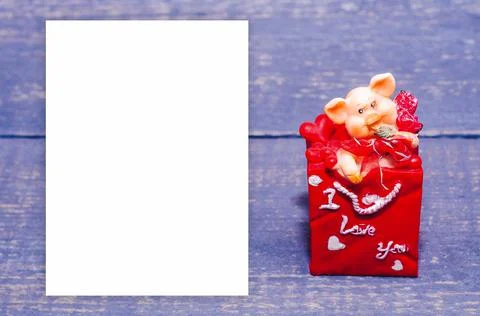 A small ceramic pig in a red envelope on a wooden background. Souvenir, gift. Stock Photos