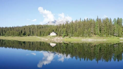 Small chalet nestled in the woods is reflected in the alpine lake. Stock Footage 133501368