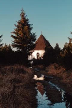 Small chapel with mountain path with puddle at sunset Stock Photos