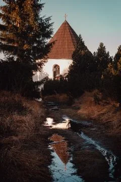 Small chapel with mountain path with puddle at sunset Stock Photos
