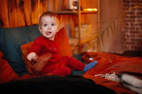 A small charming boy in a red suit is sitting on a chair Stock Photos