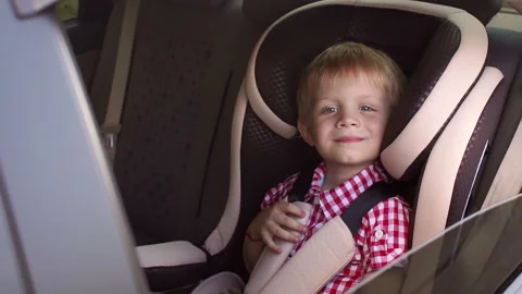 A small cheerful boy sits in a brown child car seat and shows his thumb up. Stock Footage 98887581