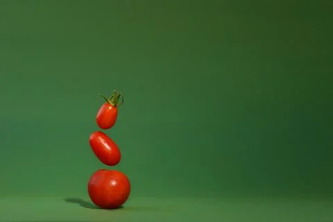 Small cherry tomatoes with a green tail in gravity on a green background Stock Photos