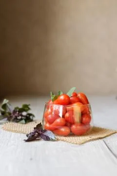 Small cherry tomatoes lie on the table in a cup with purple basel Stock Photos