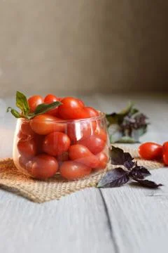 Small cherry tomatoes lie on the table in a cup with purple basel Foto stock