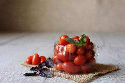 Small cherry tomatoes lie on the table in a cup with purple basel Stock Photos