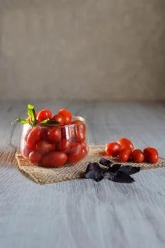 Small cherry tomatoes lie on the table in a cup with purple basel Foto stock