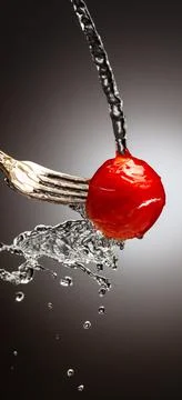 Small cherry tomatoes on a silver fork are poured with water. Splashes of water Stock Photos