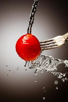 Small cherry tomatoes on a silver fork are poured with water. Splashes of water Stock Photos