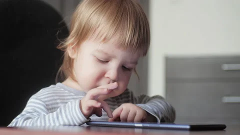 A small child of 2-3 years old sitting on a chair at the table, looking at the 库存影片 150806564
