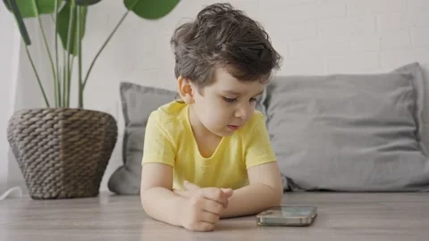 Small child 3 s watching cartoons on mobile lying on floor at home Stock Footage 245512613