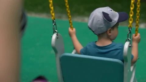 A small child, a boy sitting on a white swing with his back to the camera 스톡 동영상 108736991