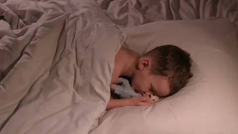 Small child boy sleeps restlessly hugging a teddy bear toy at night on bed. The Stock Footage 273569268
