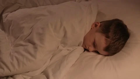 Small child boy tosses restlessly in sleep on a pillow under a blanket at night Stock Footage 273570058