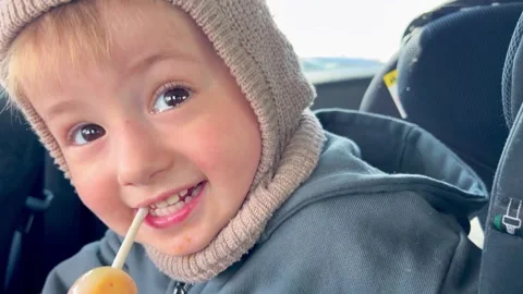 A small child with brown eyes, laughs while holding a lollipop in her mouth. Stock Footage 307128382