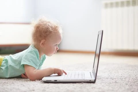 Small child at a computer lying on a carpet in a living room. Stock Photos