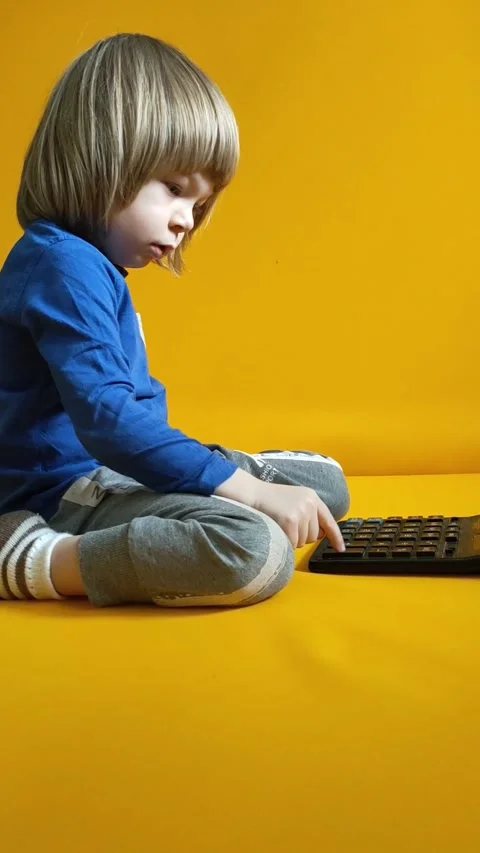 A small child counts on a calculator on a yellow background. Kid fingers press Stock Footage 280457365