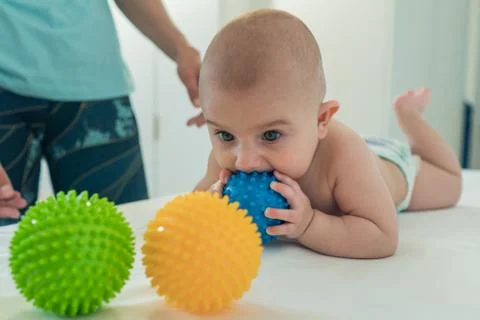 A small child crawls on the changing table and chews a rubber ball. Stock Photos