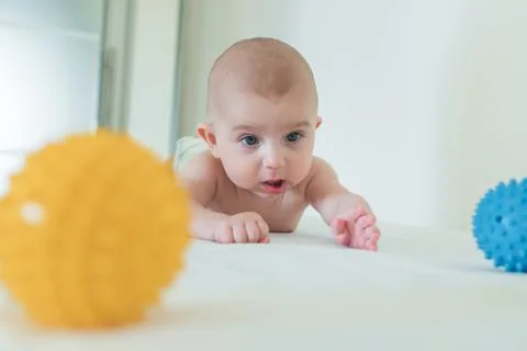 A small child crawls on the changing table and playing a rubber ball. Stock Photos