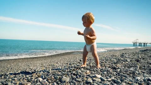 A small child in a diaper alone on the beach plays with stones and raises his Stock Footage 169302941