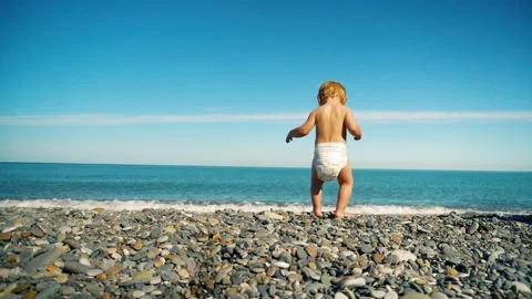 A small child in a diaper alone on the seashore, playing with stones with his Stock Footage 169302913
