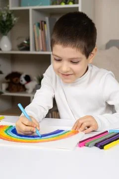 A small child draws a rainbow with felt-tip pens in a sketchbook while sitting Photos