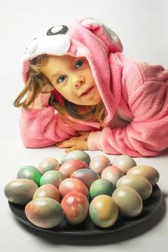 A small child dressed as an Easter bunny is guarded by a plate with colored eggs Stockfoto's