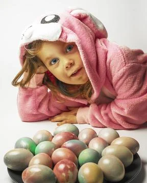A small child dressed as an Easter bunny is guarded by a plate with colored eggs Stock Photos