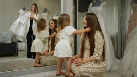 Small child dressed in white is smiling while standing next to her mother inside Stock Footage 264093826
