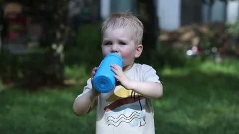 A small child drinks water from a bottle and offers it Stock Footage 157236965