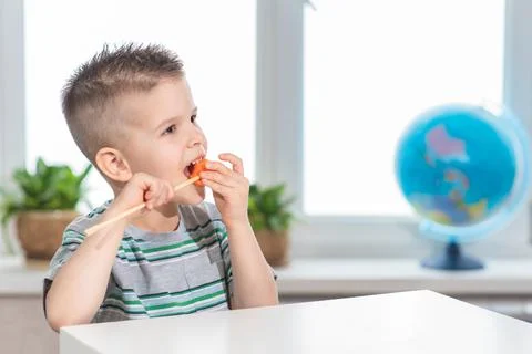 A small child eats a carrot on a stick at home. The boy is eating vegetables  Stock Photos