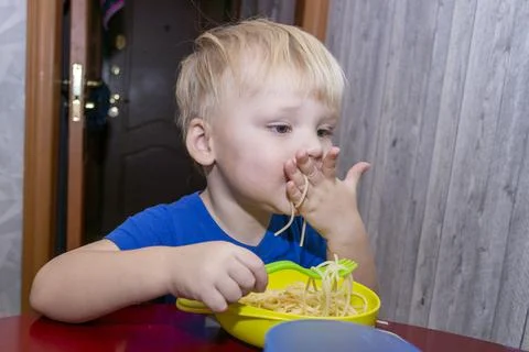 A small child eats noodles in the kitchen, Stock Photos