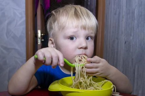 A small child eats noodles in the kitchen, Stock Photos
