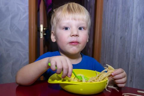 A small child eats noodles in the kitchen, Stock Photos