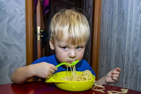 A small child eats noodles in the kitchen, Stock Photos