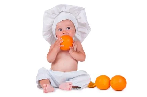 A small child eats an orange slice in a chef suit on a white background. Stock Photos