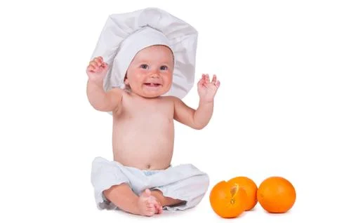 A small child eats an orange slice in a chef suit on a white background. Stock Photos