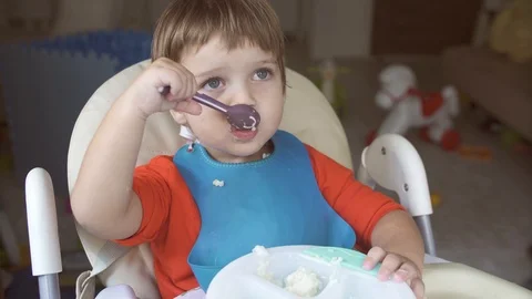 A small child eats porridge sitting in a child's chair Stock Footage 120821763
