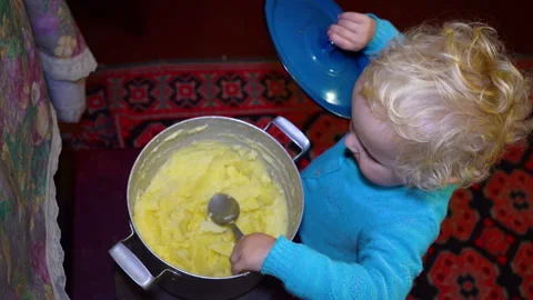 A small child eats potatoes from a pot with his hands Stock Footage 333299556
