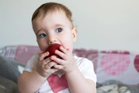 Small child eats a red apple at home closeup. Stock-Fotos