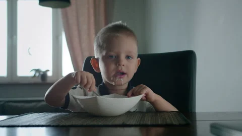 A small child eats with a spoon on his own. He's all dirty and focused Stock Footage 130490225