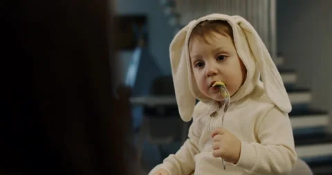 A small child, fed by his mother with avocado in the kitchen, a hungry child. Stock Footage 149070876