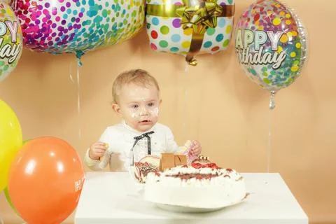 A small child at the festive table eats a cake. Stock Photos