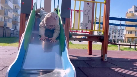 A small child goes down a slide on his stomach, a toddler plays on a playground. Stock Footage 306254429