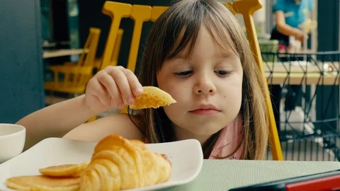 A small child has breakfast in the hotel restaurant. Girl eats croissant and  Stock Footage 104188770