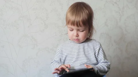A small child holding a digital tablet and tapping the screen of an electronic Stock Footage 151695190