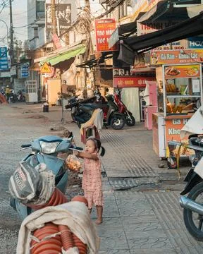 A small child holds snacks while standing between parked motorbikes on a bu.. Stock Photos