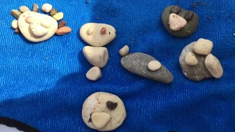 Small child laying out shingle pebbles on beach. Funny mugs are obtained from Stock Footage