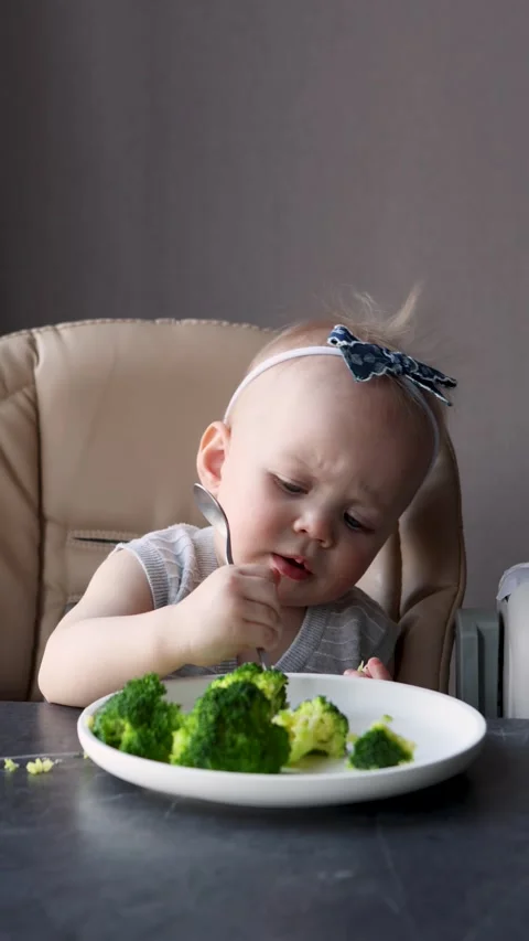 Small child learning to feed herself with spoon, eating healthy broccoli at Stock Footage 311440809